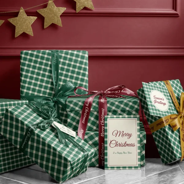 Stack of presents in evergreen gingham paper with ribbons and a Merry Christmas card by a burgundy wall