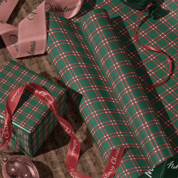 Rolls of green windowpane plaid gift wrap and a wrapped box with satin ribbons on a wooden floor