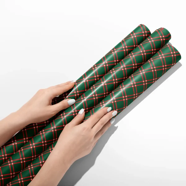 Hands smoothing three rolls of green windowpane plaid wrapping paper on a white table