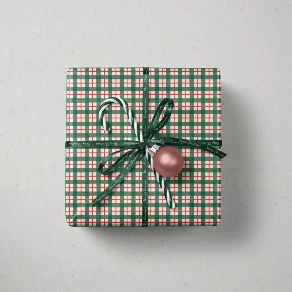 Top view of a gift in green and red check paper with a ribbon, candy canes and a bauble