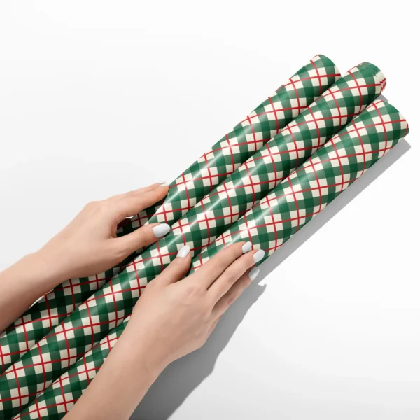 Hands smoothing three rolls of green and red check wrapping paper on a white table