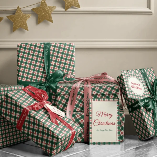 Stack of presents in green and red check paper with ribbons and a Merry Christmas card by a cream wall