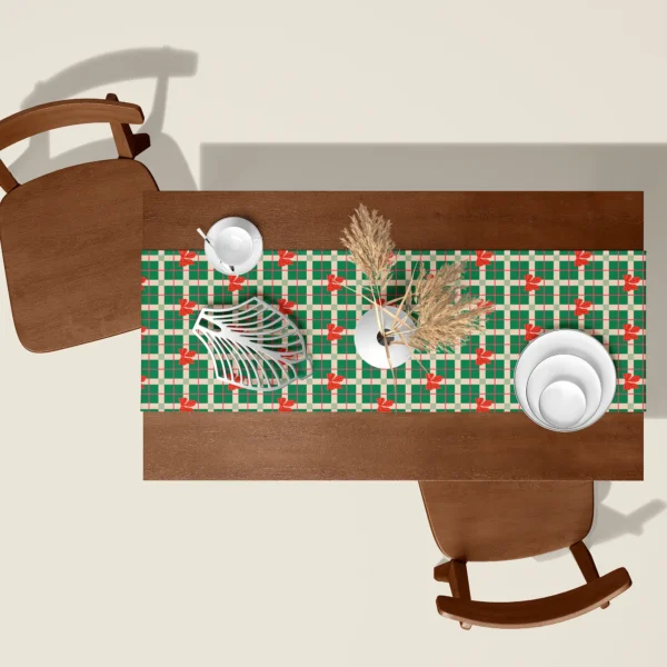 Green plaid with red bows Christmas table runner seen from above on a walnut table with white dishes and dried pampas