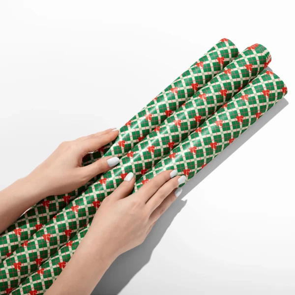 Hands smoothing three rolls of green plaid bow wrapping paper on a white table