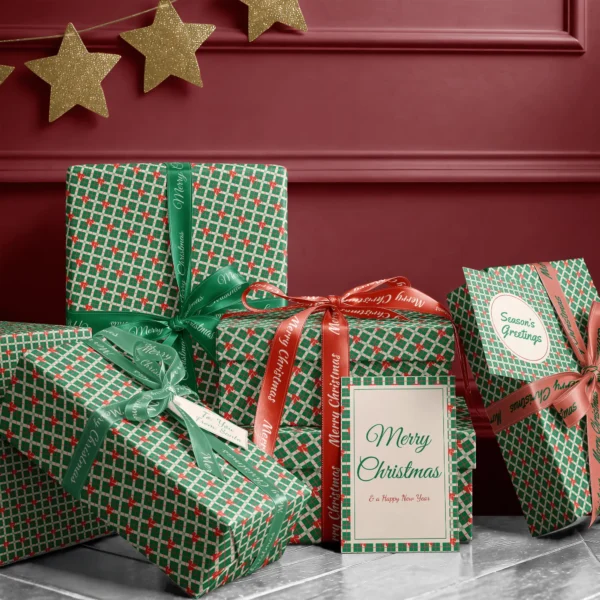 Stack of presents in green plaid bow paper with ribbons and a Merry Christmas card by a burgundy wall