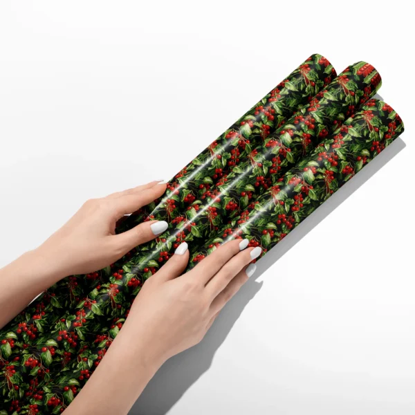Hands smoothing three rolls of black holly berry wrapping paper on a white table