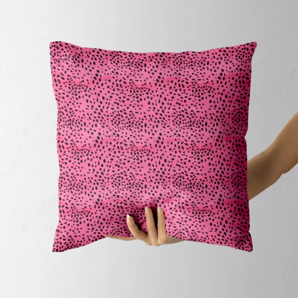 Hand holding the square hot pink pillow with black spots