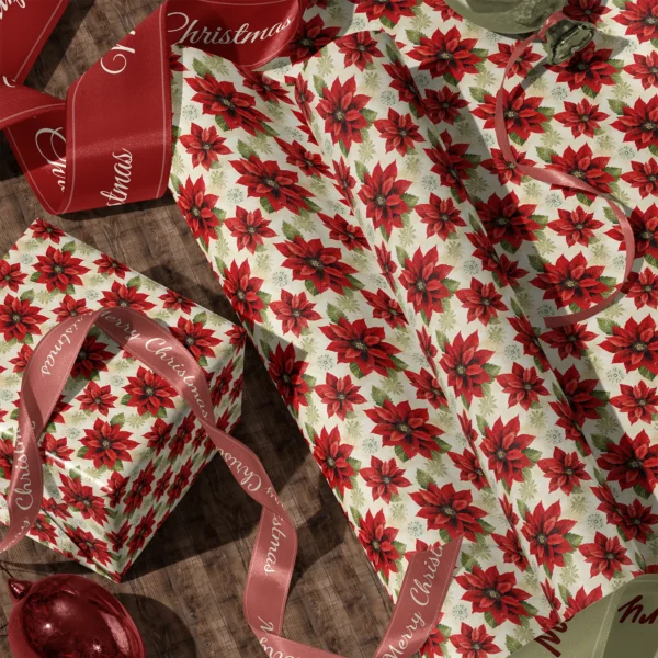 A sheet of large cream poinsettia gift wrap and a wrapped box with satin ribbons on a wooden floor