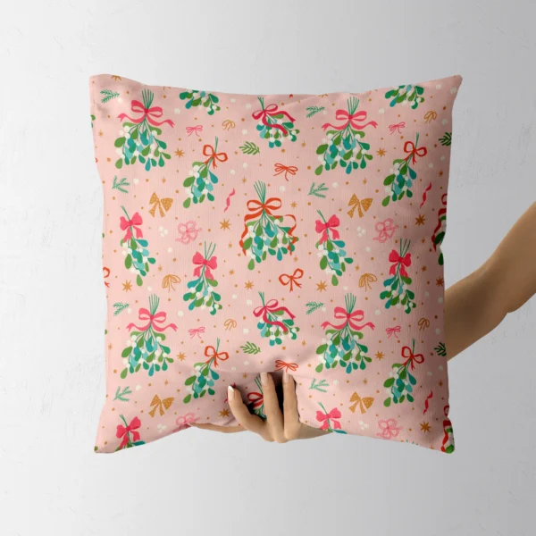 A hand holding the pink pillow printed with mistletoe and bows