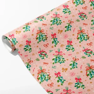 Roll of blush pink wrapping paper with mistletoe bunches tied in pink bows and gold stars, partly unrolled on white