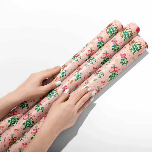 Hands smoothing three rolls of mistletoe wrapping paper on a white table
