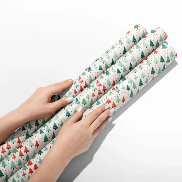 Hands smoothing three rolls of white dotted tree wrapping paper on a white table