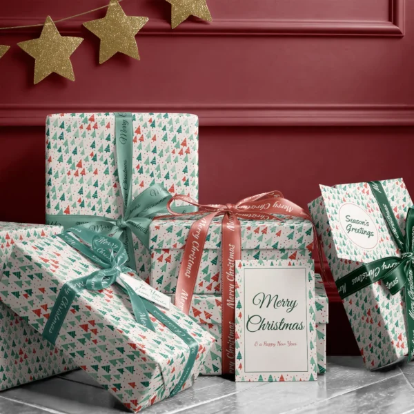 Stack of presents in white dotted tree paper with ribbons and a Merry Christmas card by a burgundy wall