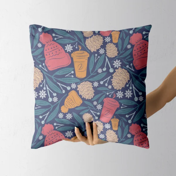 A hand holding the navy pillow with beanies and hot drink cups