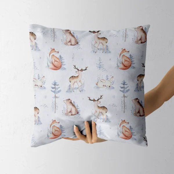 A hand holding the pale blue pillow with watercolor forest animals
