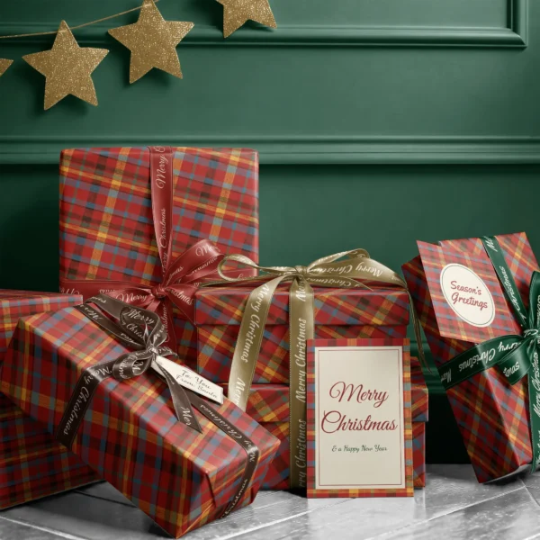 Stack of presents in patchwork plaid paper with ribbons and a Merry Christmas card by a dark green wall