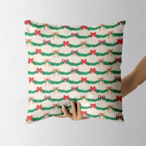 Hand holding the cream pillow printed with pine swags and red bows