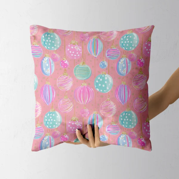 A hand holding the coral-pink bauble throw pillow