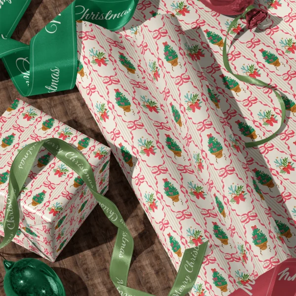 Rolls of pink ribbon frame gift wrap and a wrapped box with satin ribbons on a wooden floor