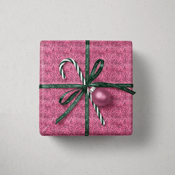 Top view of a gift in hot pink spotted paper with a ribbon, a candy cane and a bauble