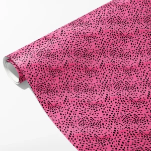 Roll of hot pink wrapping paper covered in swirling black spots of different sizes, partly unrolled on white