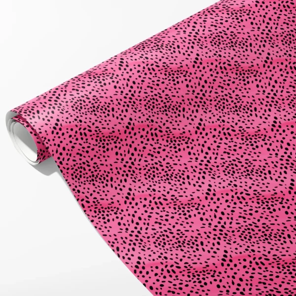 Roll of hot pink wrapping paper covered in swirling black spots of different sizes, partly unrolled on white