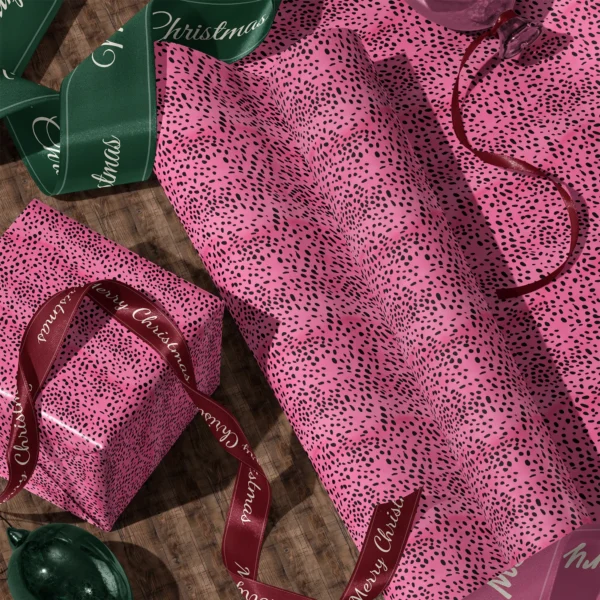 A sheet of hot pink spotted gift wrap and a wrapped box with satin ribbons on a wooden floor