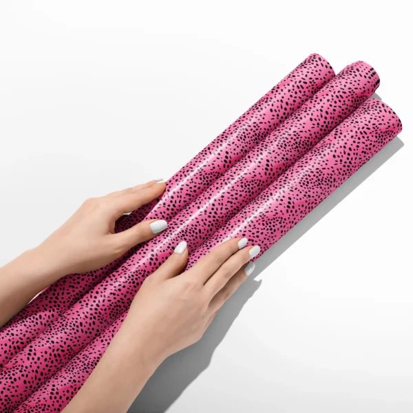 Hands smoothing three rolls of hot pink spotted wrapping paper on a white table