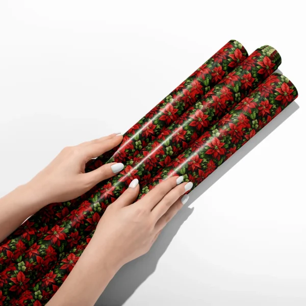 Hands smoothing three rolls of dark green poinsettia wrapping paper on a white table