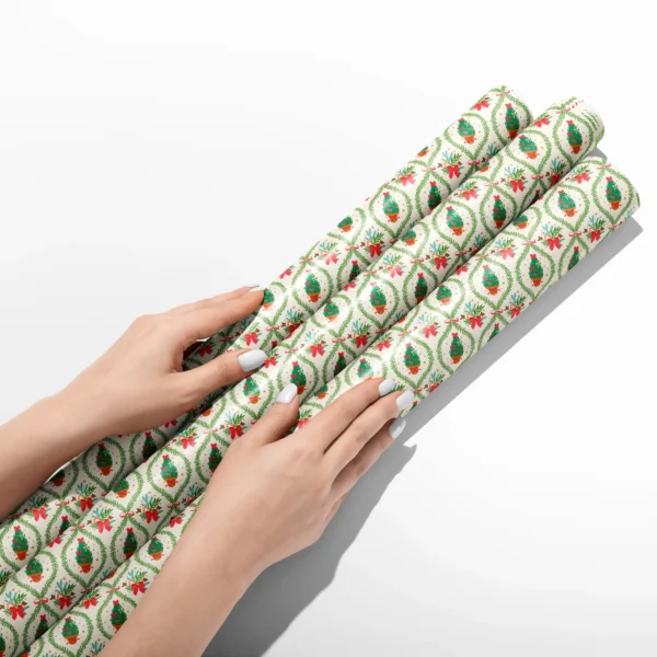 Hands smoothing three rolls of potted tree lattice wrapping paper on a white table