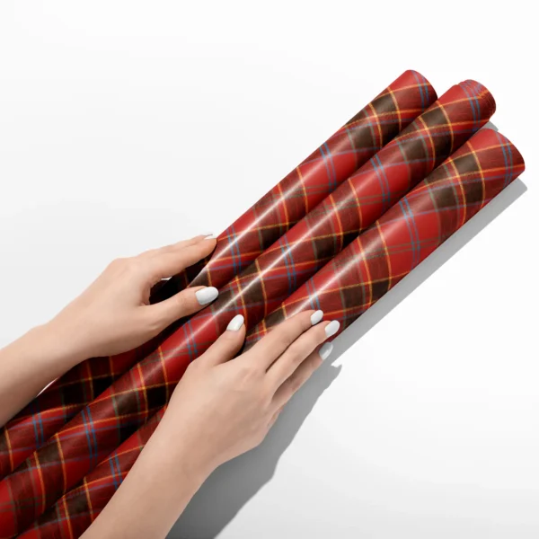 Hands smoothing three rolls of red and black block plaid wrapping paper on a white table