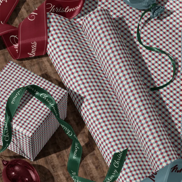 A sheet of red and blue gingham gift wrap and a wrapped box with satin ribbons on a wooden floor