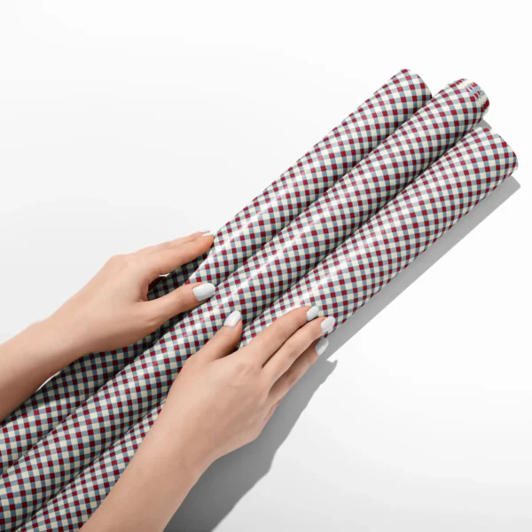 Hands smoothing three rolls of red and blue gingham wrapping paper on a white table