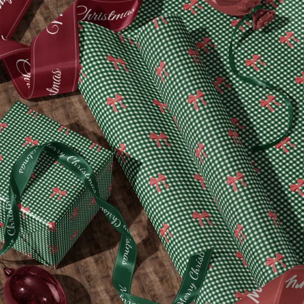 Rolls of red bow gingham gift wrap and a wrapped box with satin ribbons on a wooden floor