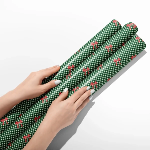 Hands smoothing three rolls of red bow gingham wrapping paper on a white table