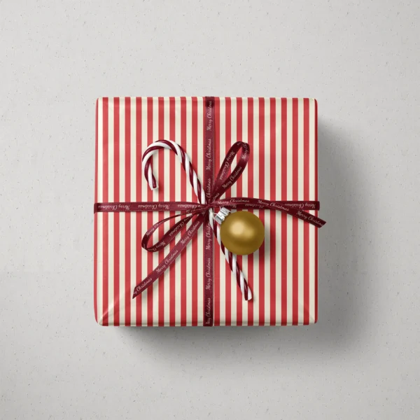 Top view of a gift in red cabana stripe paper with a ribbon, candy canes and a bauble