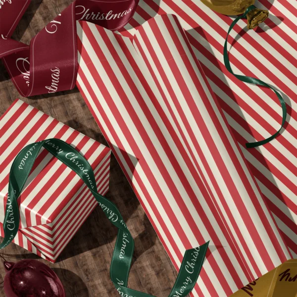Rolls of red cabana stripe gift wrap and a wrapped box with satin ribbons on a wooden floor