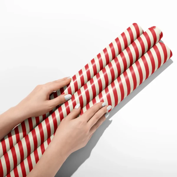 Hands smoothing three rolls of red cabana stripe wrapping paper on a white table