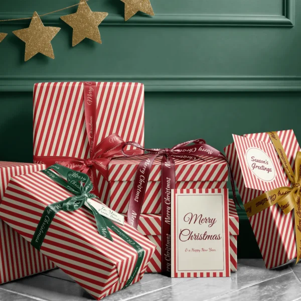 Stack of presents in red cabana stripe paper with ribbons and a Merry Christmas card by a dark green wall