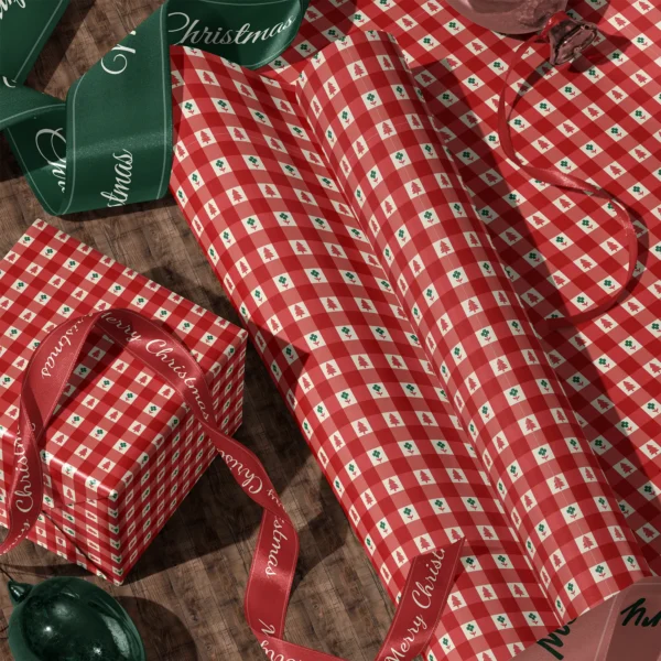 Rolls of red gingham tree gift wrap and a wrapped box with satin ribbons on a wooden floor