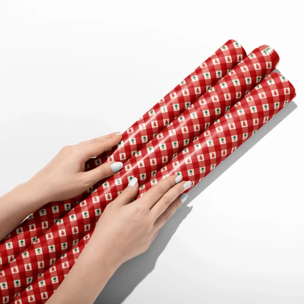 Hands smoothing three rolls of red gingham tree wrapping paper on a white table