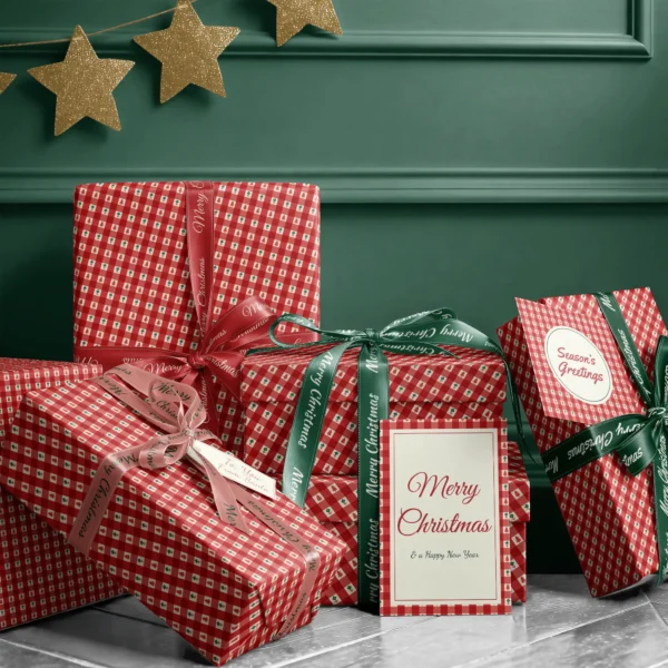 Stack of presents in red gingham tree paper with ribbons and a Merry Christmas card by a dark green wall