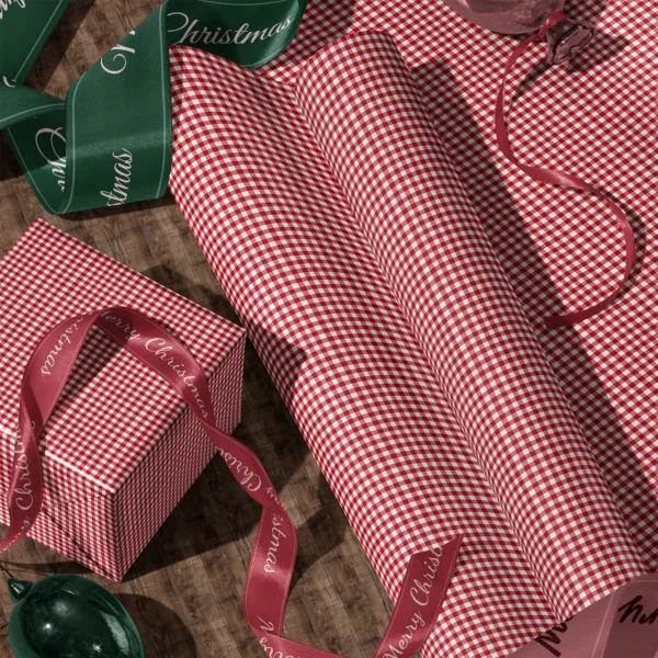 A sheet of red gingham gift wrap and a wrapped box with satin ribbons on a wooden floor