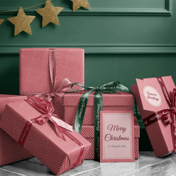 Stack of presents in red gingham paper with ribbons and a Merry Christmas card by a dark green wall
