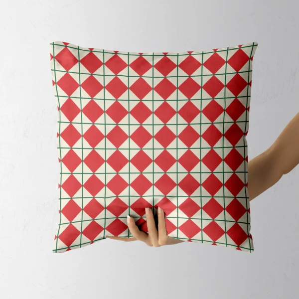A hand holding the red diamond throw pillow with green lattice