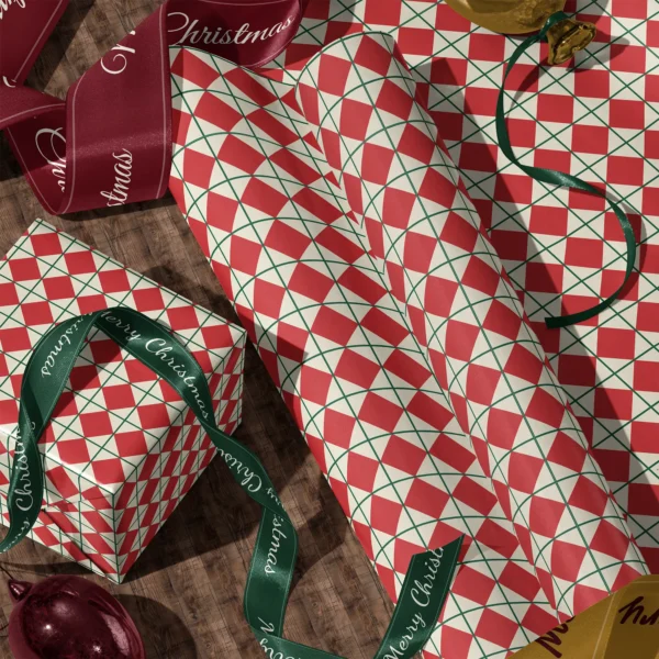 Rolls of red harlequin gift wrap and a wrapped box with satin ribbons on a wooden floor