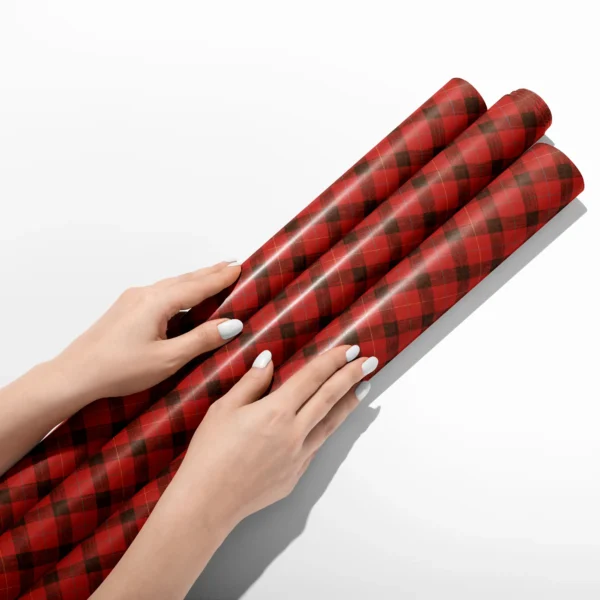Hands smoothing three rolls of red lumberjack check wrapping paper on a white table