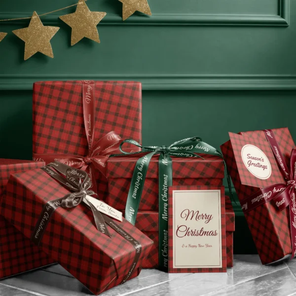 Stack of presents in red lumberjack check paper with ribbons and a Merry Christmas card by a dark green wall