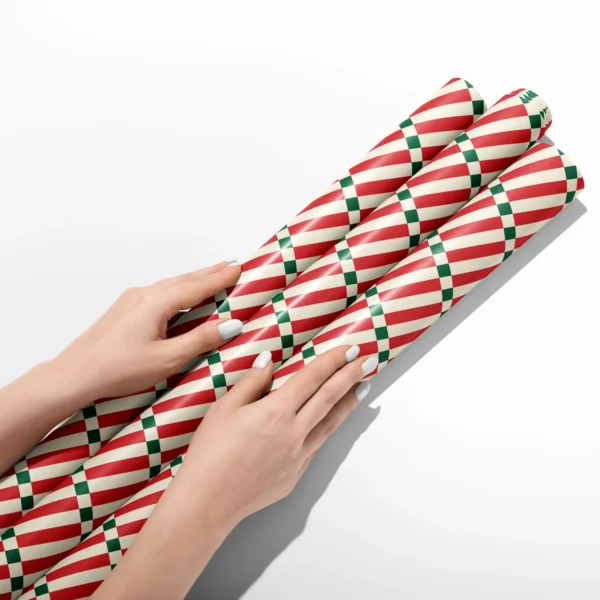 Hands smoothing three rolls of red stripe ladder wrapping paper on a white table