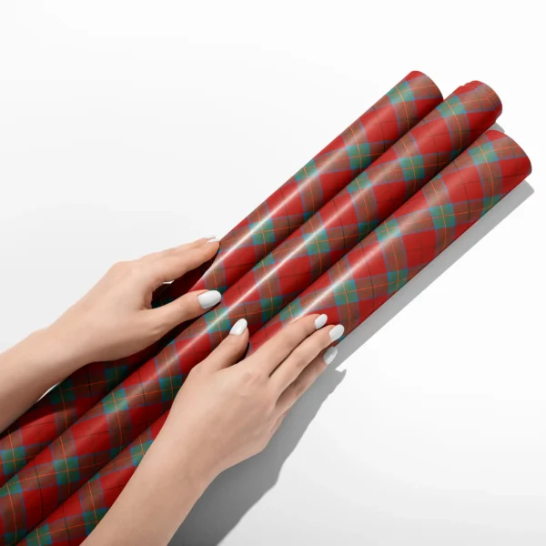Hands smoothing three rolls of red and teal windowpane plaid wrapping paper on a white table